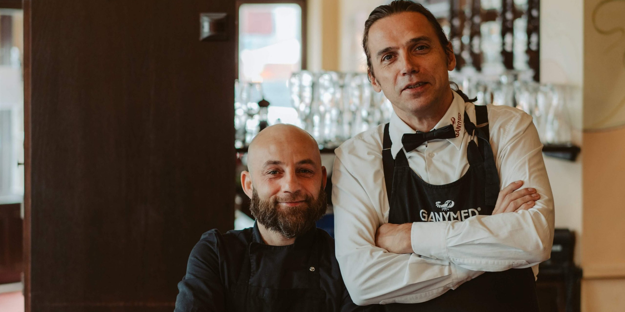 Zwei Mitarbeiter des Ganymed, links Küchenchef Pietro Solito, rechts Chefkellner André Stockhausen, fotografiert vor der Theke der Ganymed Brasserie.