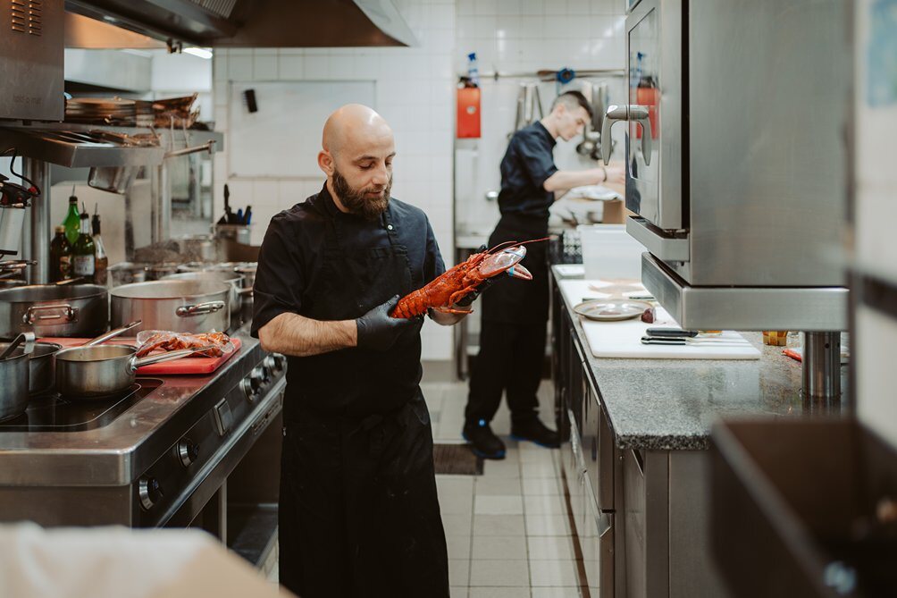 Chef Pietro Solito is holding a lobster in his hand in the kitchen of the Ganymed Brasserie Berlin.